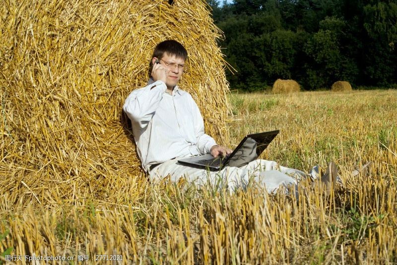 外国帅哥坐在草堆边玩笔记本的人物图片
