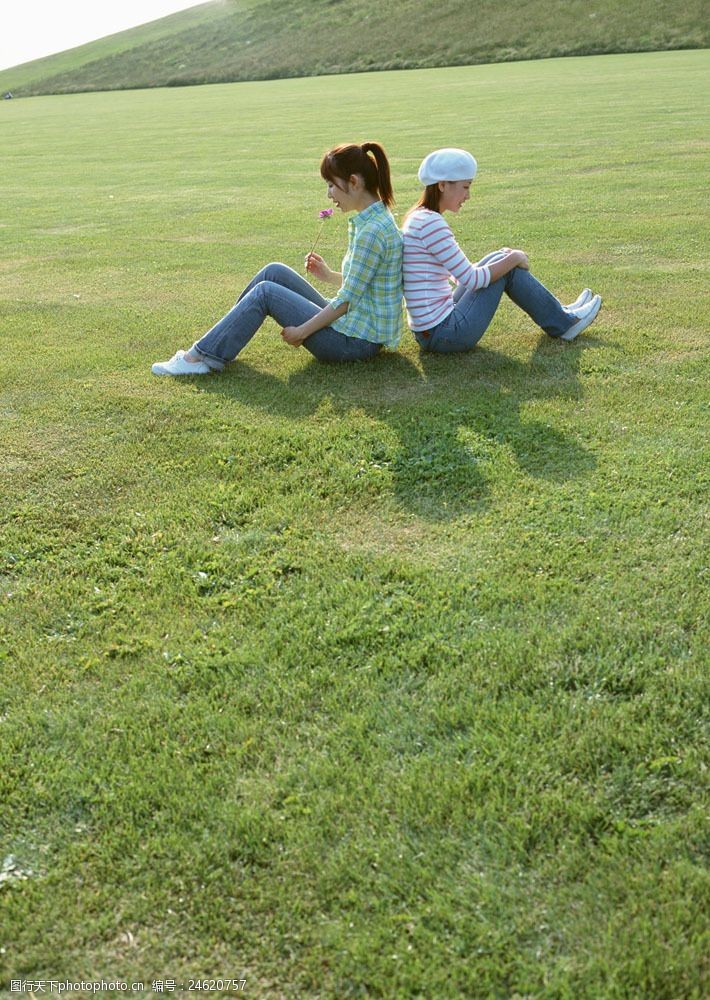 假日休闲女性背靠背坐在草地上的两美女图片