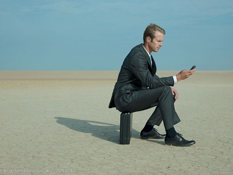 蓝色领子在沙漠中坐着皮箱玩手机的外国商业男人图片