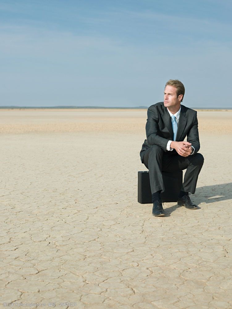 气候在沙漠中坐在皮箱上的商业男人图片